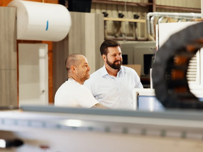 Two men stand in front of a factory machine, engaged in discussion about its operation and maintenance.