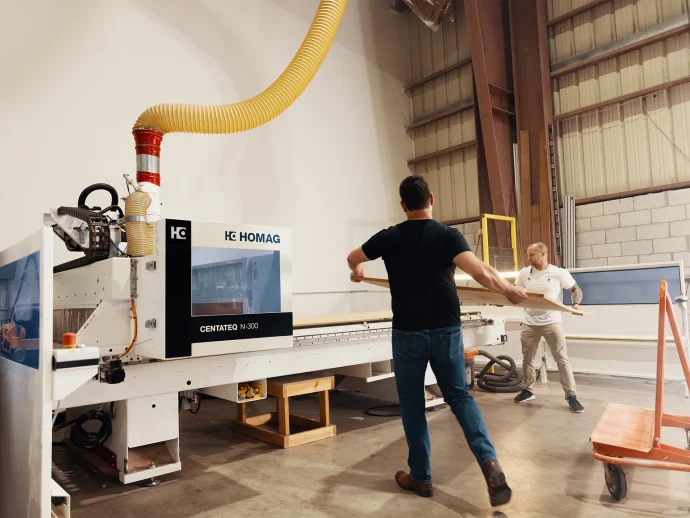 Two individuals engaged in woodworking, utilizing a machine to craft wooden materials in a workshop setting.
