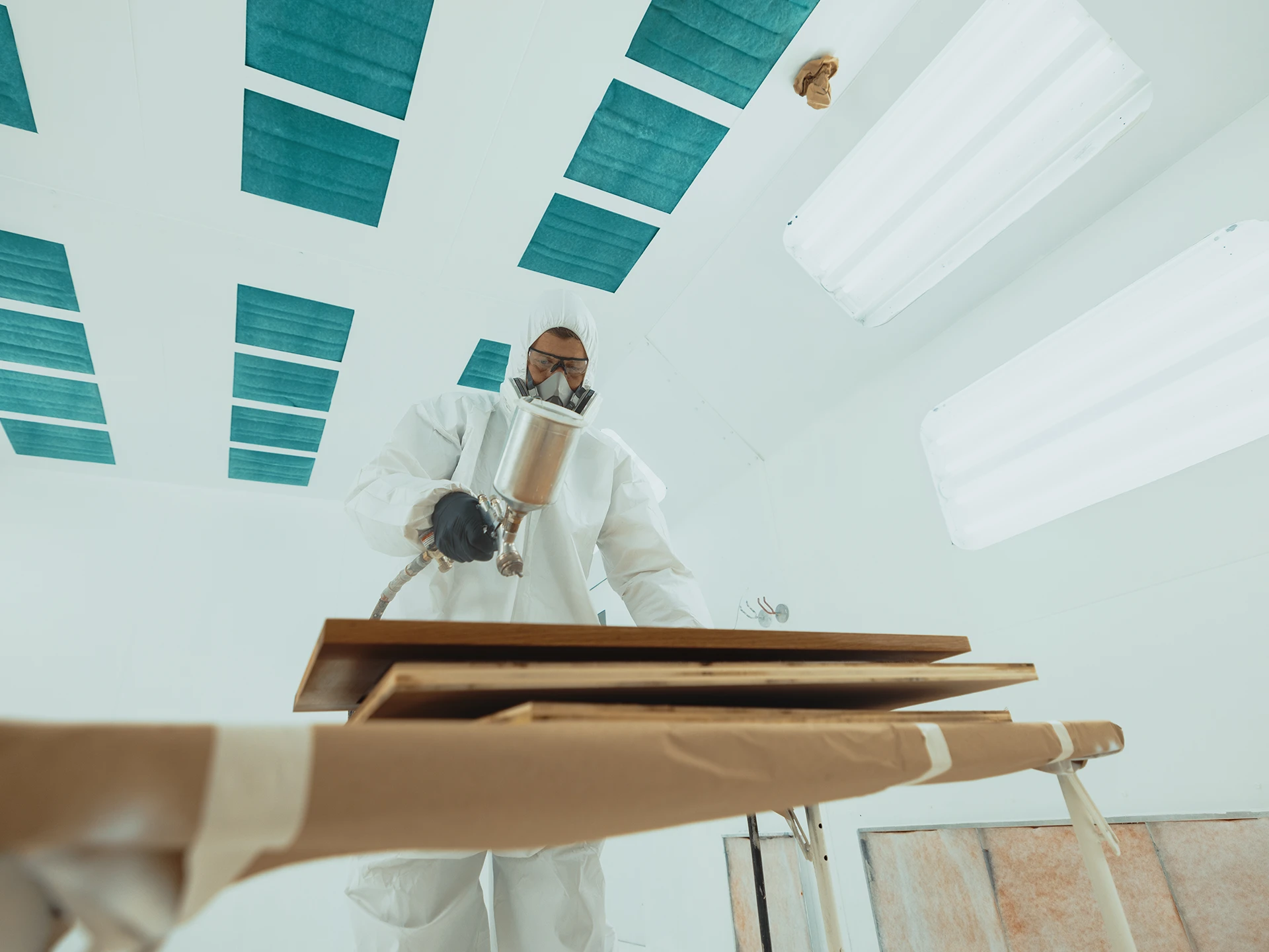 Man in a white protective suit and mask applies paint to a wooden table.