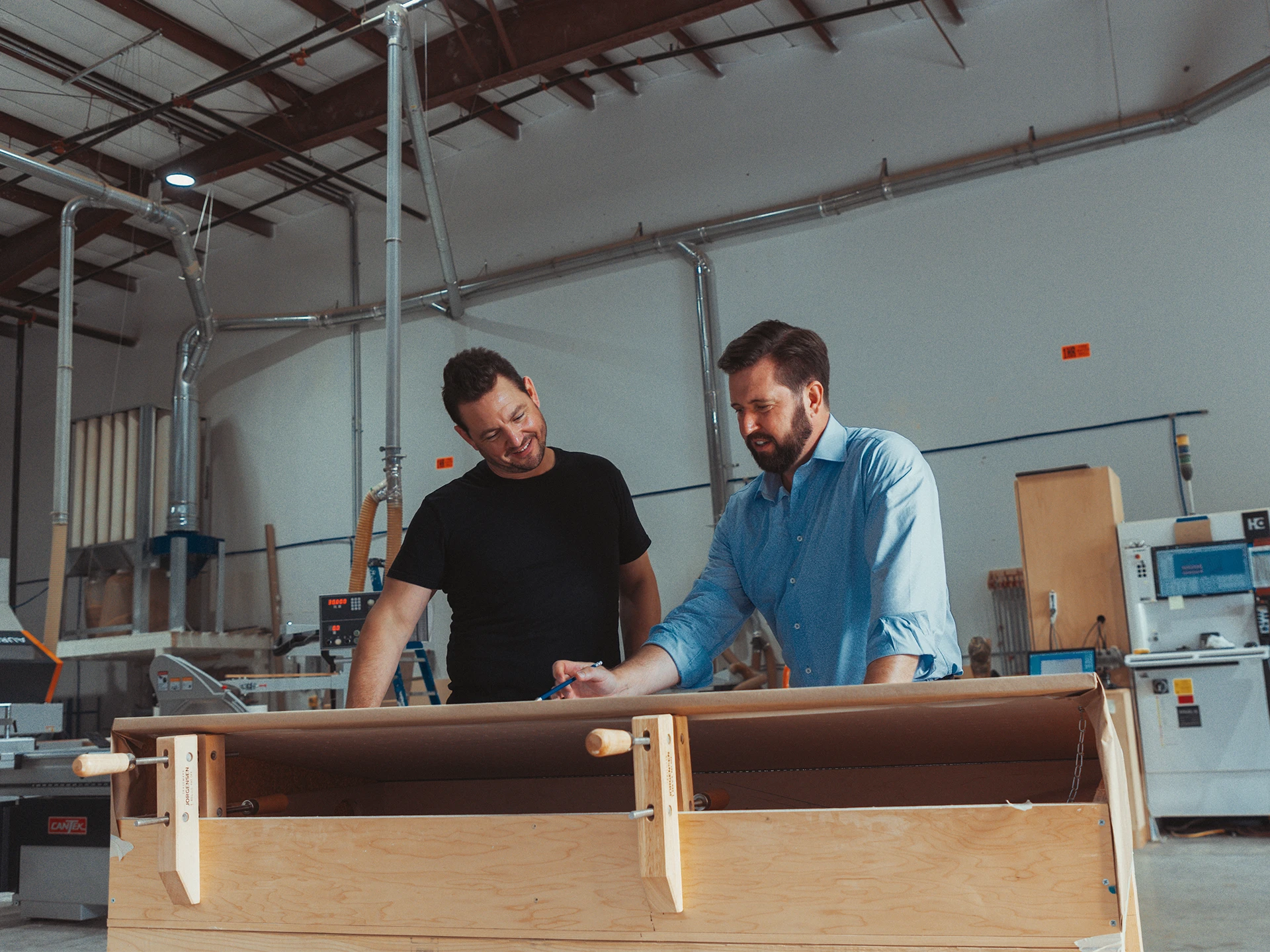 Two men working diligently on a wooden table, utilizing tools and materials for their project.