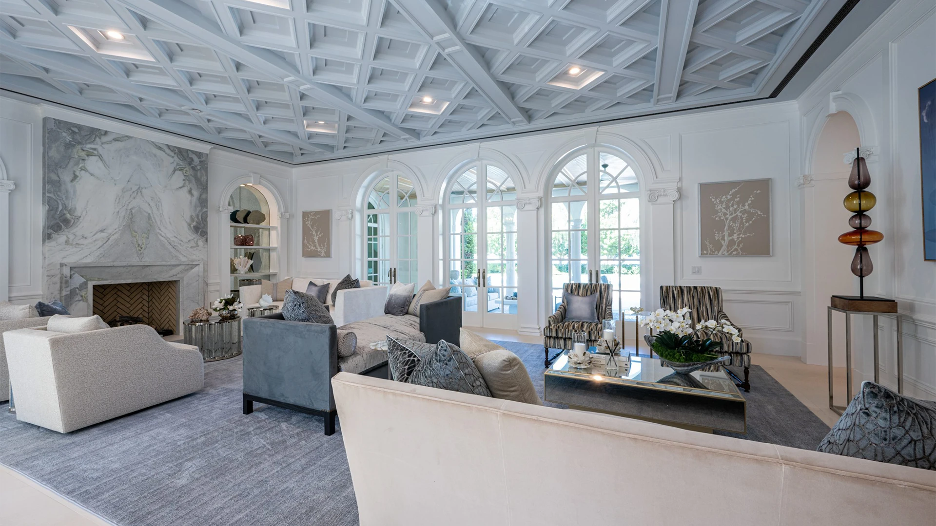 Sophisticated living room adorned with white furnishings, a warm fireplace, and grey accents and bright windows.