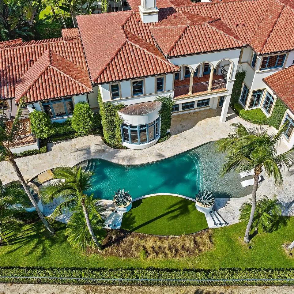 Captivating aerial image of a luxury New Mediterranean style property, featuring a glistening pool and surrounded by exquisite landscaping.