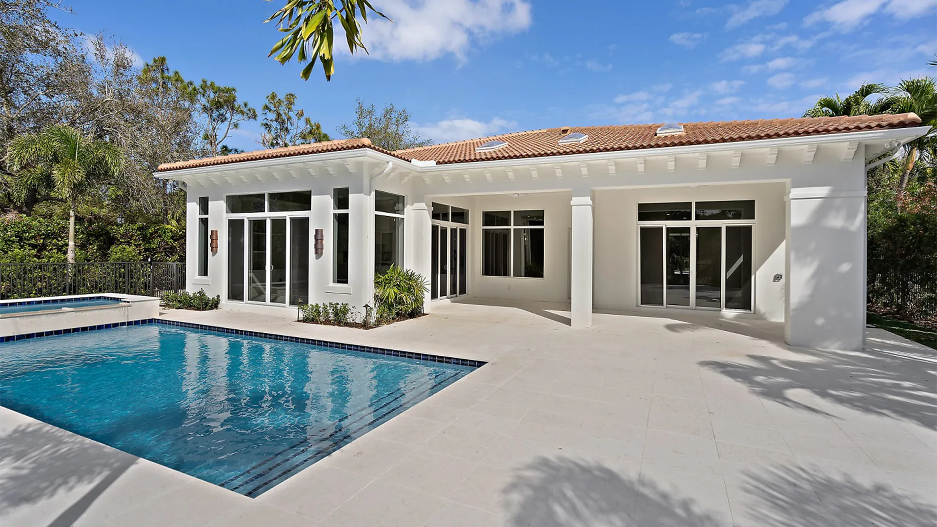 Exquisite pool reflects the sophistication of an opulent Coastal Contemporary style house, surrounded by elegant palm trees under a bright blue sky.
