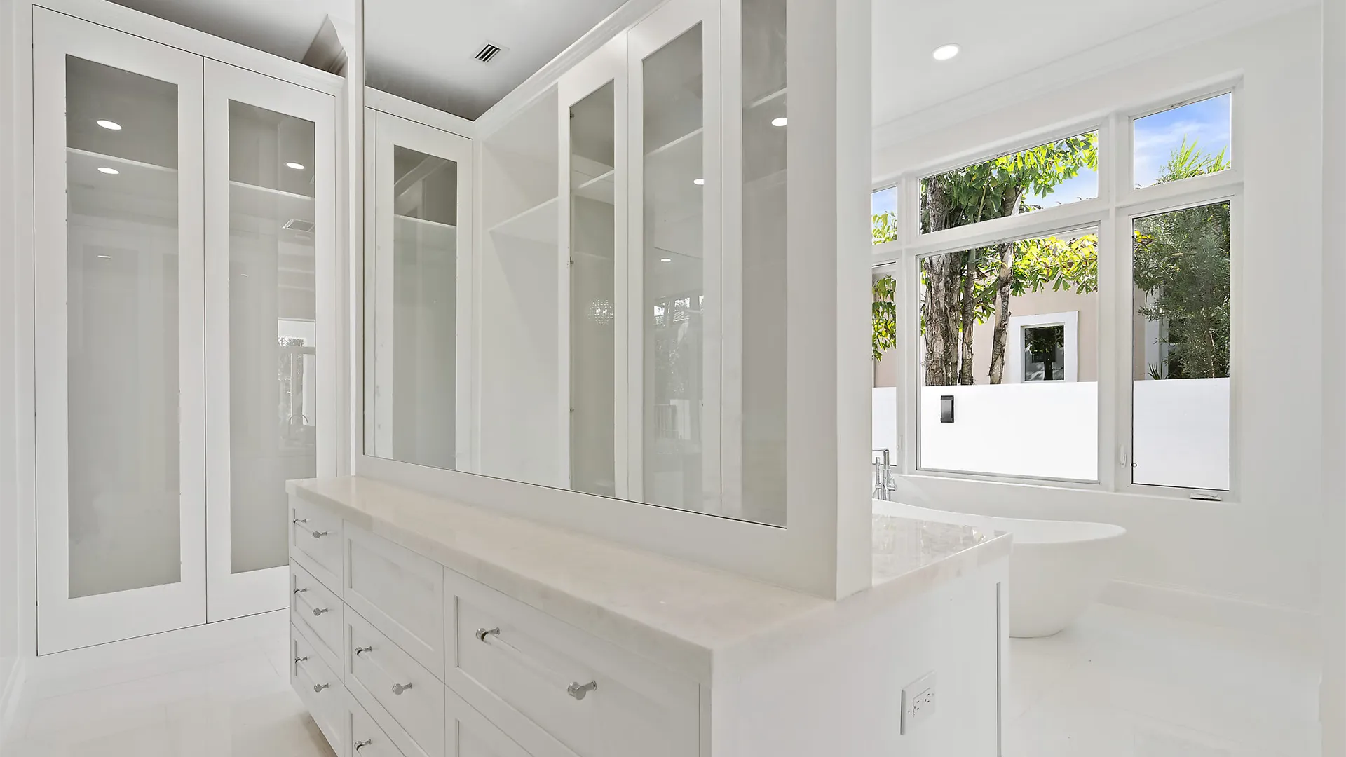 Pristine white bathroom highlighted by a large mirror and a comfortable tub.