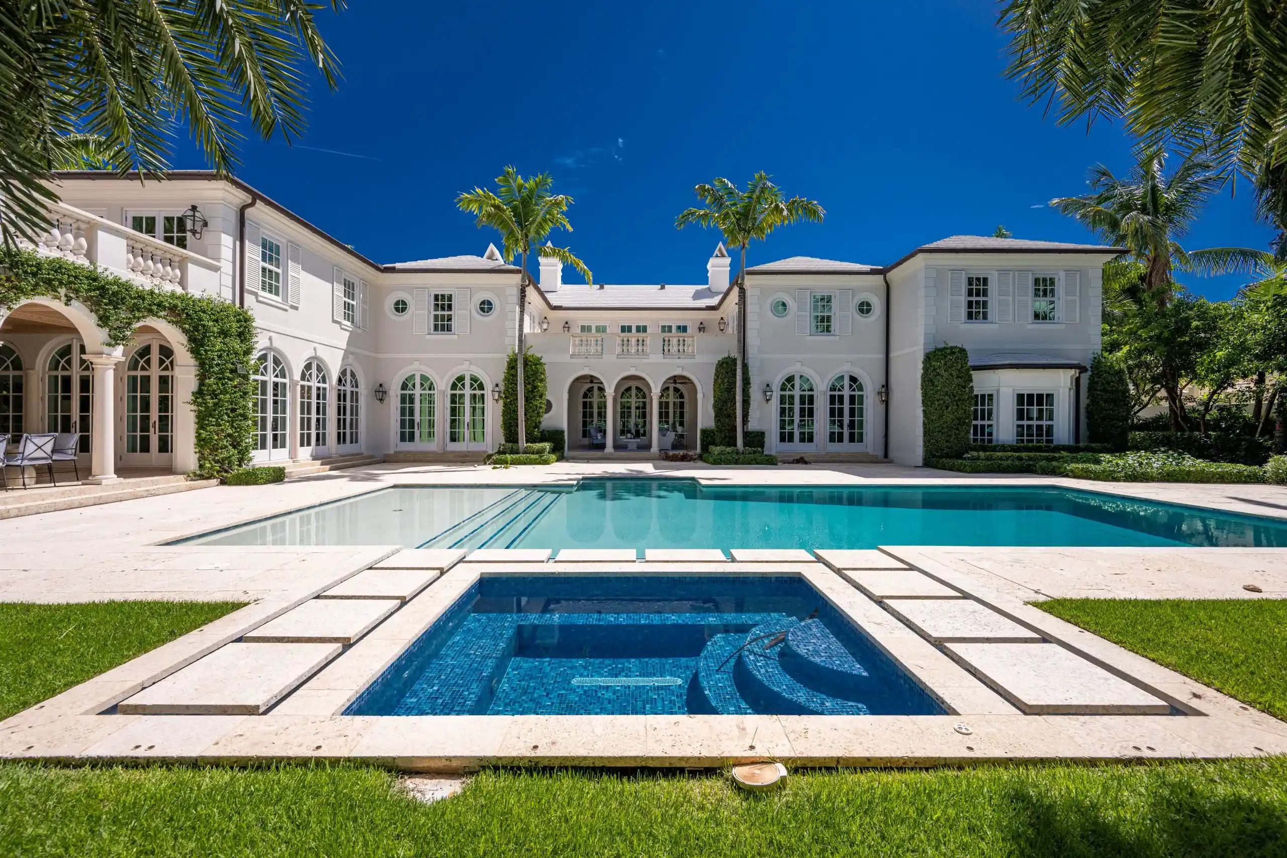 Elegant white Bermuda Colonial style mansion with a luxurious pool, embraced by palm trees.