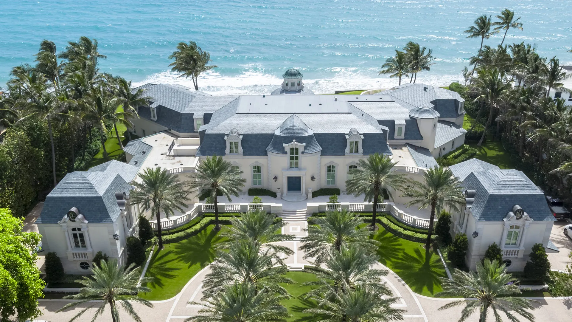 Aerial shot of a luxury French Normandy style mansion by the beach, revealing its majestic design and idyllic seaside location.