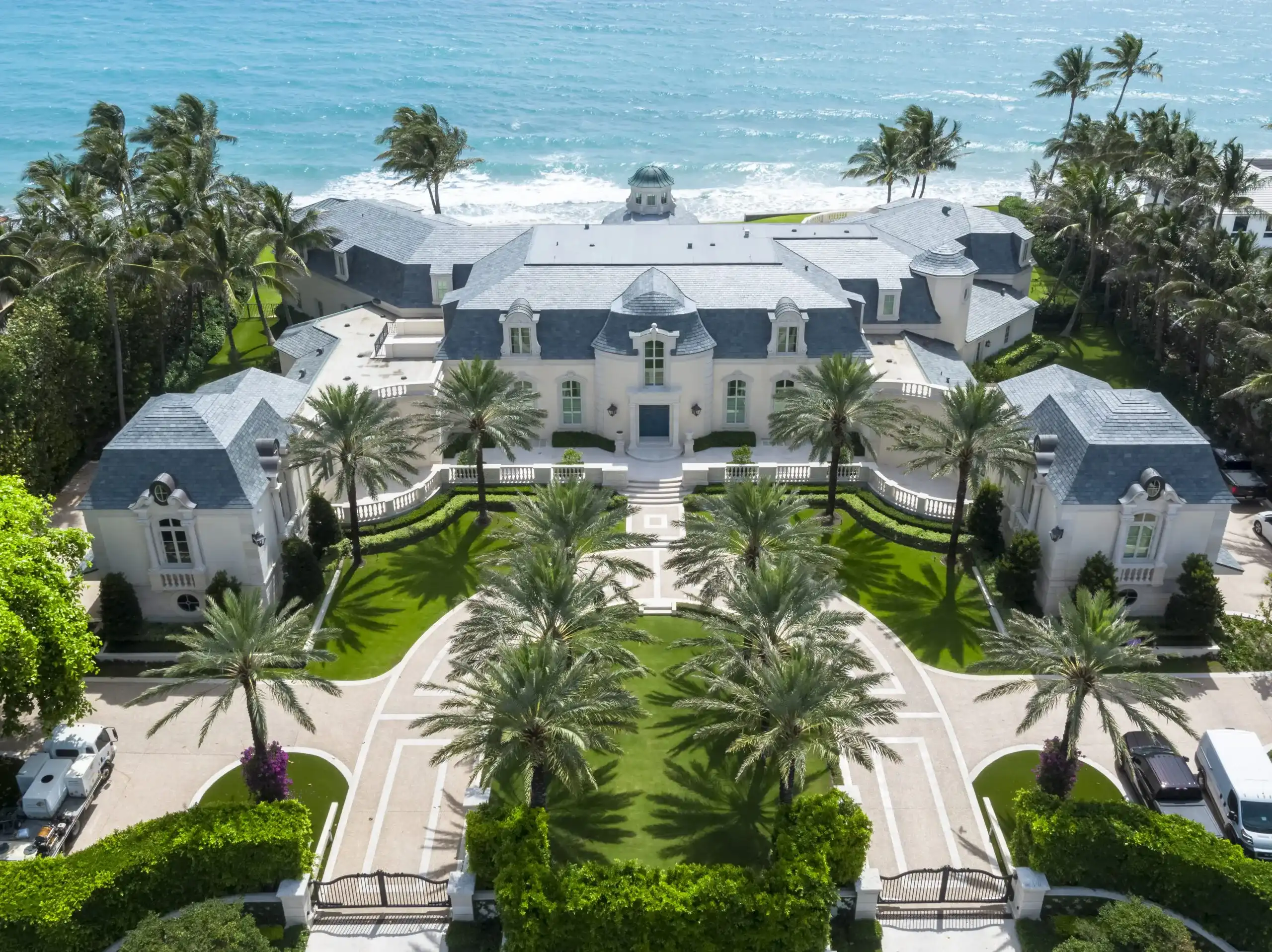 Aerial shot of a luxury French Normandy style mansion by the beach, revealing its majestic design and idyllic seaside location.