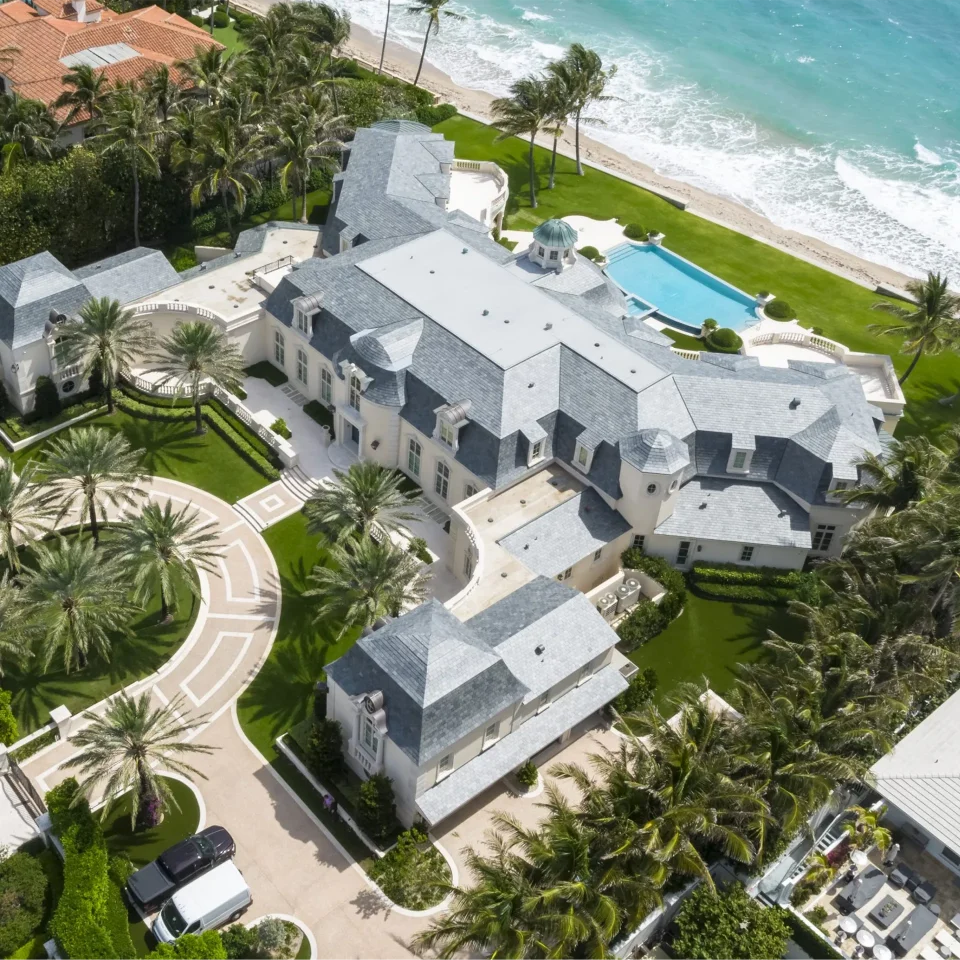 Aerial shot of a luxury French Normandy style mansion by the beach, revealing its majestic design and idyllic seaside location.