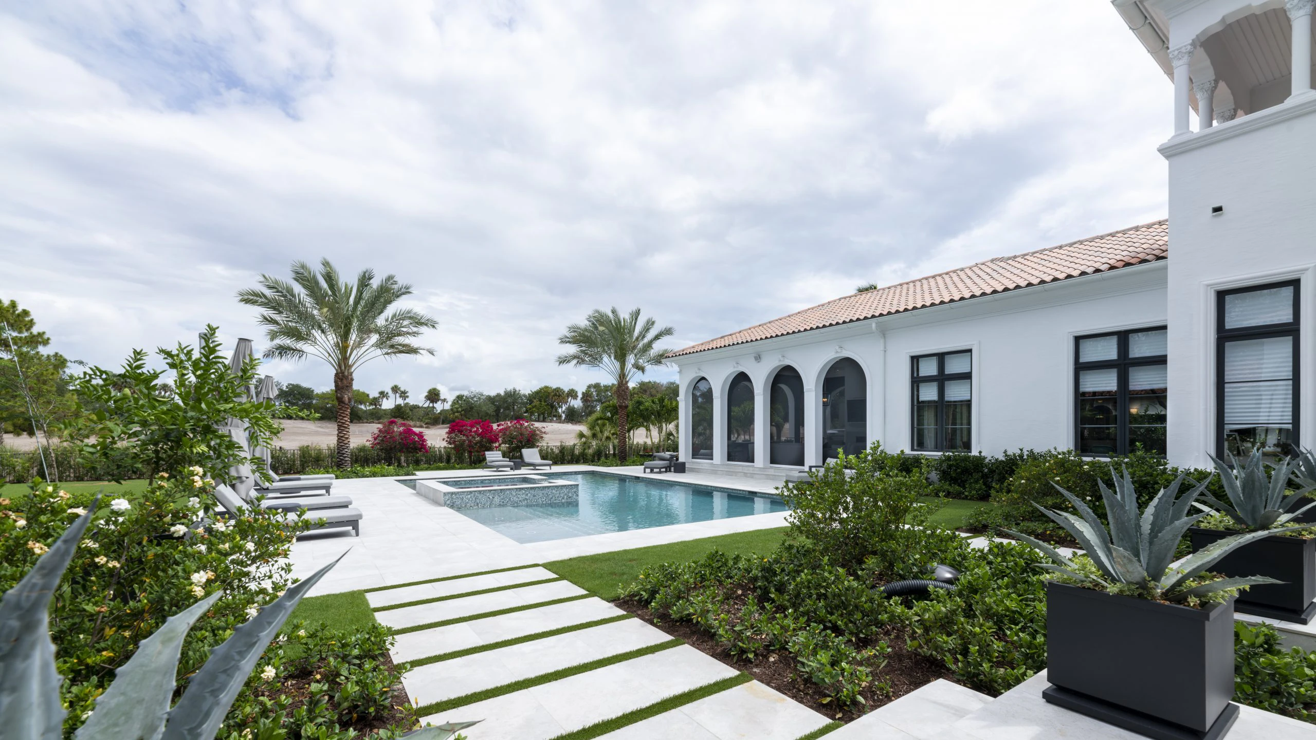 Beautiful white Modern Mediterranean home showcasing a pool and patio, surrounded by chairs for enjoying sunny days outdoors.