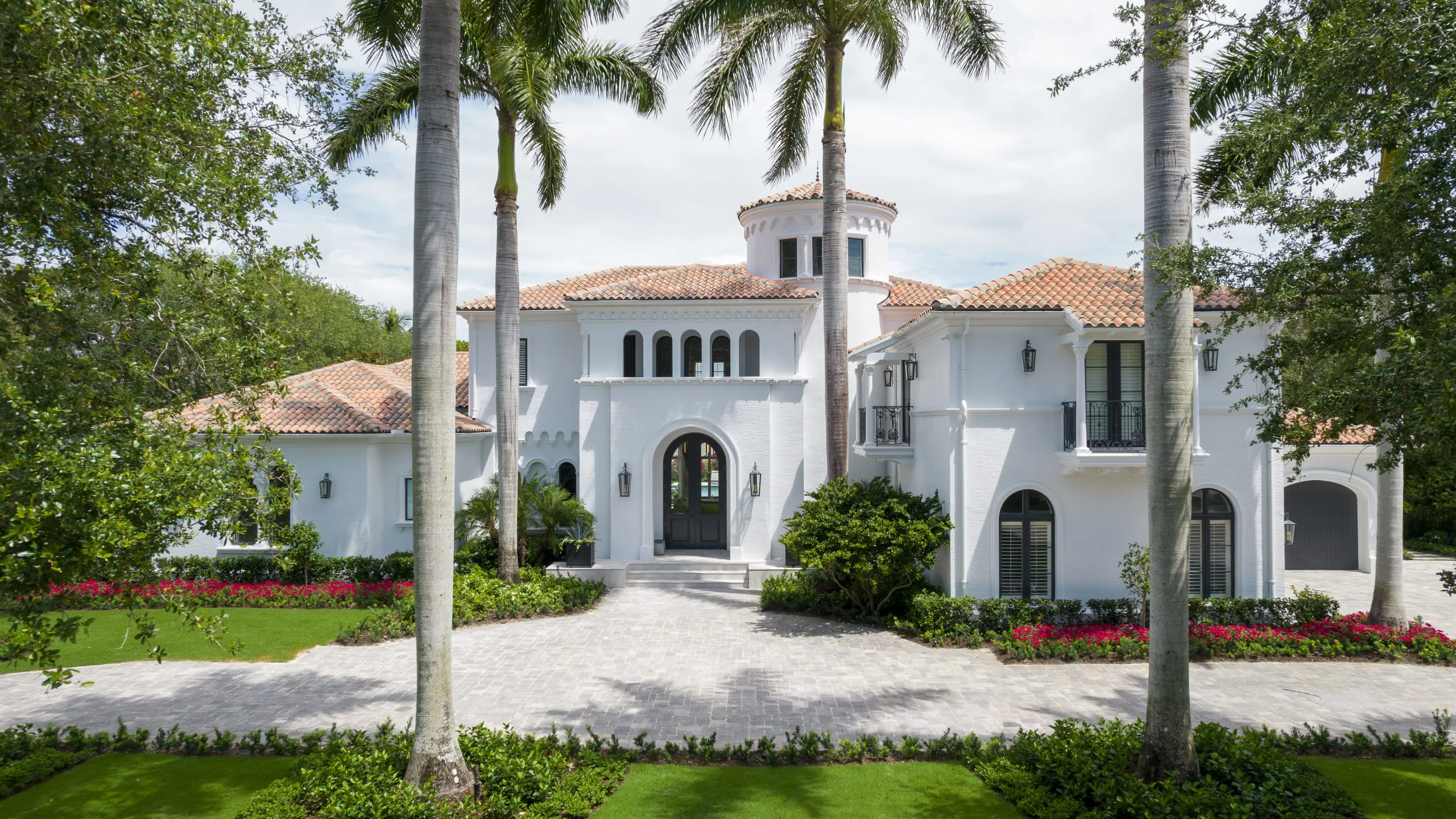 White Modern Mediterranean style mansion with palm trees and a lush green lawn, epitomizing luxury living in a serene environment.