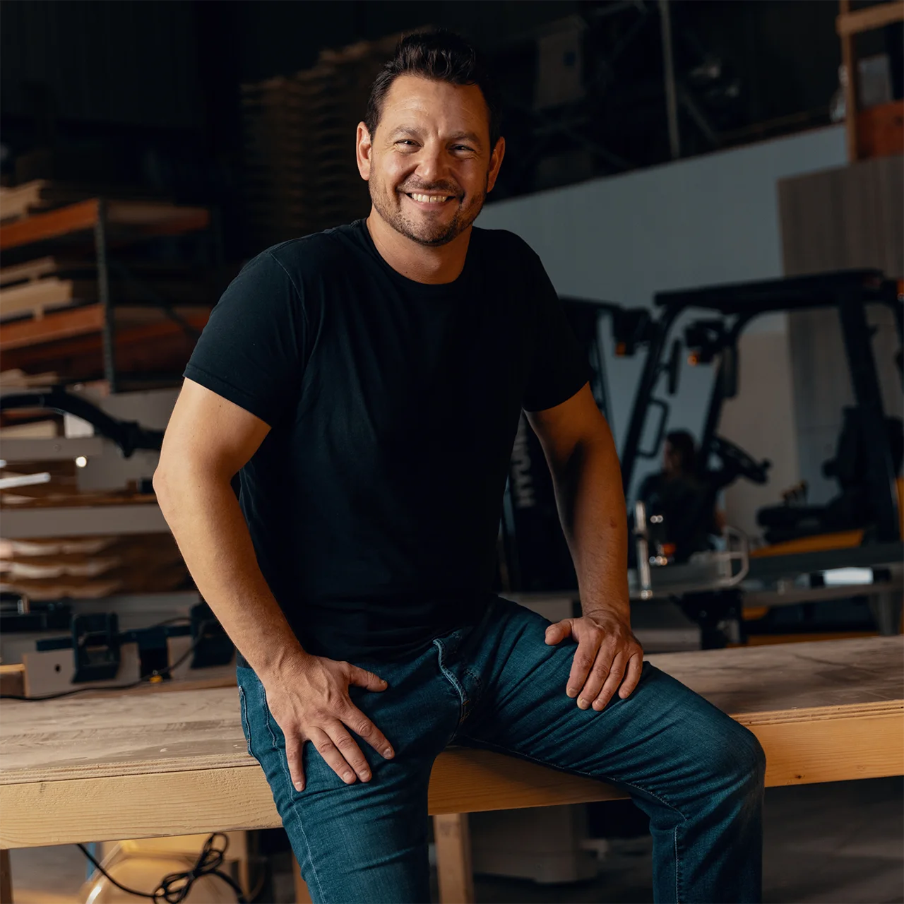 Portrait of Josh Burgess sitting on top of wooden table inside the workshop.