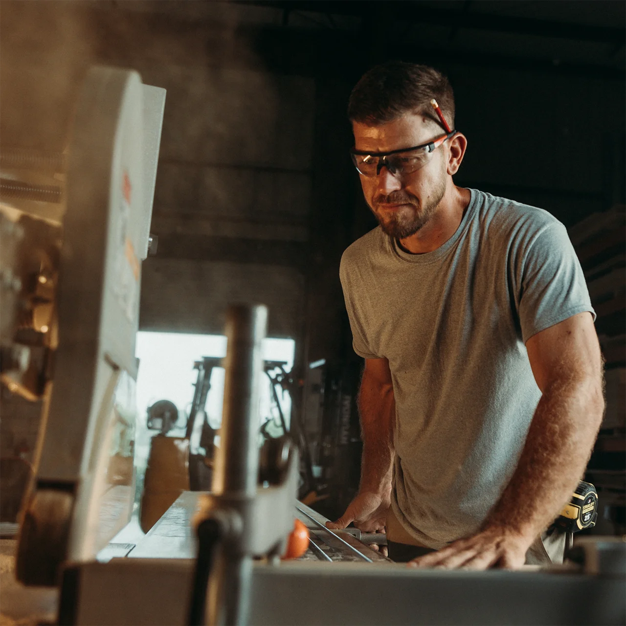 Man wearing glasses operates a table saw inside a workshop.