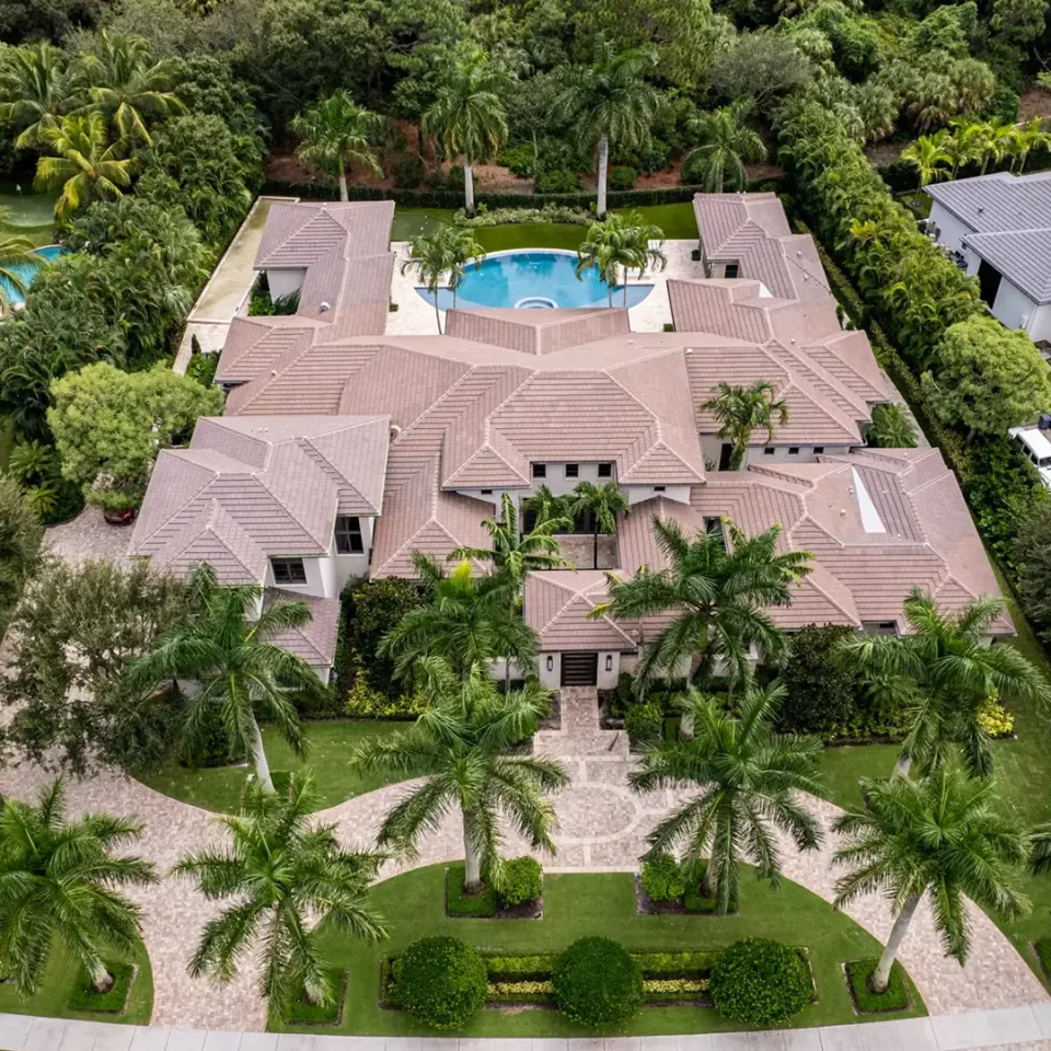 Elevated view of an Coastal Contemporary style exquisite home, encircled by flourishing palm trees and a pristine pool, showcasing a rich green oasis.