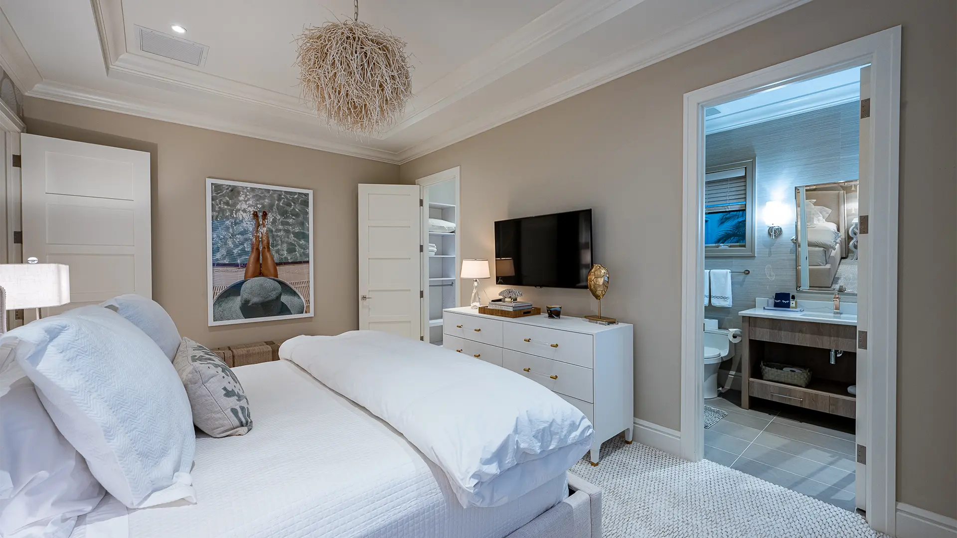 Refined bedroom enhanced by calming beige walls and a chic lamp, a white bed and television.
