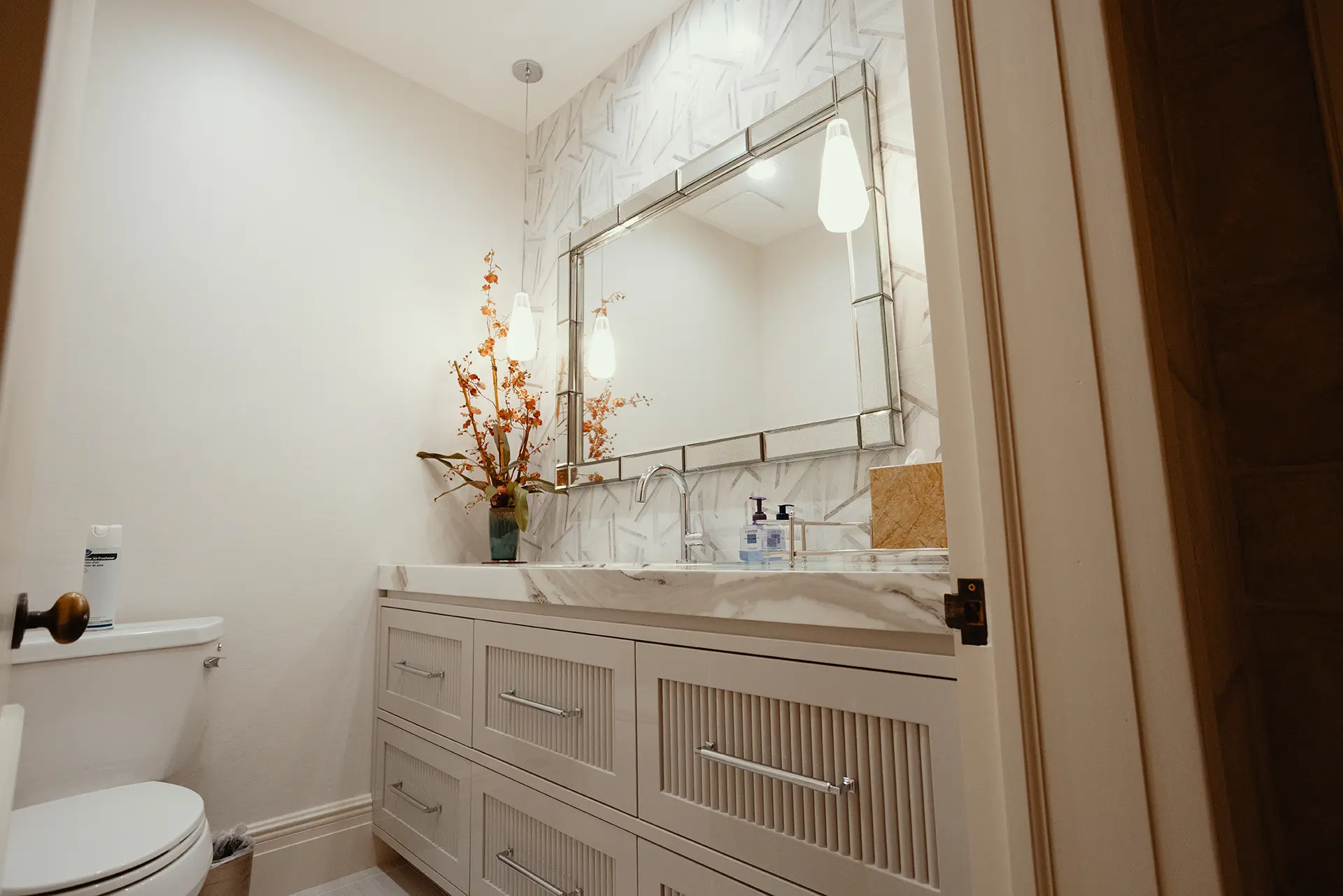 Bright bathroom scene highlighting a white toilet, 3-inch mitered Calacatta marble with decorations and silver mirror.